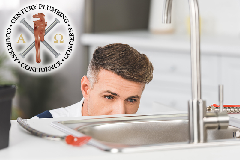 A Century Plumbing technician inspecting a kitchen faucet under a sink.
